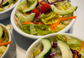 Several Bowls Of Fresh Salad Containing Lettuce, Cucumber Slices, Cherry Tomatoes, Shredded Carrots, And Purple Cabbage, Arranged On A White Surface.