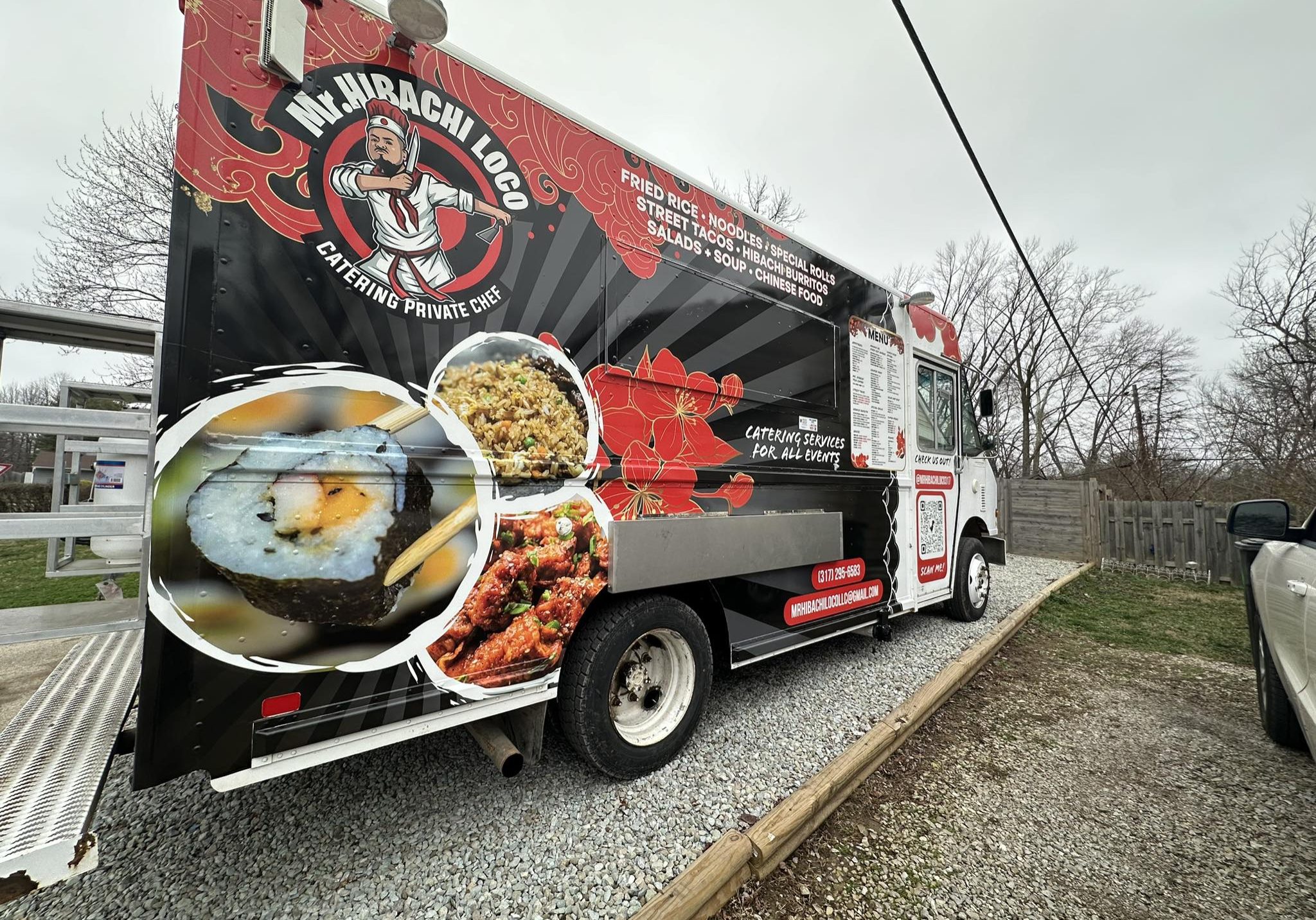 A Vibrant Food Truck Painted With Colorful Graphics Advertising Hibachi And Latin Inspired Dishes, Parked On A Gravel Lot Under An Overcast Sky.